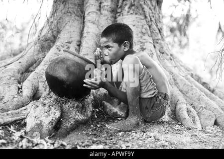 Indianerjunge Trinkwasser aus einem Tontopf auf Banyanbaum. Andhra Pradesh, Indien. Schwarz / weiß Stockfoto