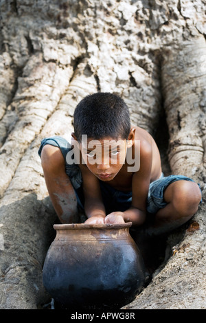 Indianerjunge Trinkwasser aus einem Tontopf auf Banyanbaum. Andhra Pradesh, Indien Stockfoto