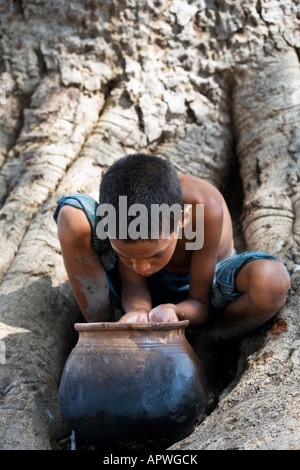 Indianerjunge Trinkwasser aus einem Tontopf auf Banyanbaum. Andhra Pradesh, Indien Stockfoto