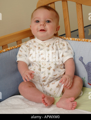 Ein vier Monate altes Baby setzt sich in seinem Bettchen Stockfoto