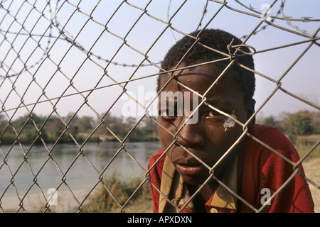 Ein close-up Portrait eines schweren lokalen jungen spähte durch einen Drahtzaun in einem Dorf Divundu Stockfoto