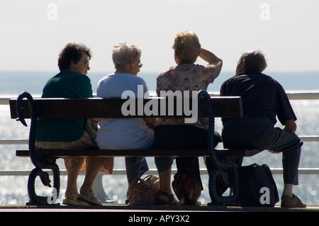 Rückansicht der vier mittleren Alter Menschen sitzen auf einer Bank Aberystwyth Promenade mit Blick auf die Cardigan Bay, Sommernachmittag UK Stockfoto