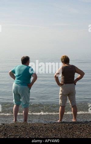 eine Rückansicht von zwei Frauen stehen mit den Händen auf den Hüften Paddeln im Meeresstrand Aberystwyth Ceredigion Wales UK Sommernachmittag Stockfoto