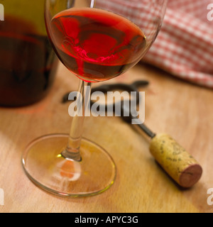NAHAUFNAHME VON ROTEN ROSE WEIN NEBEN KORKENZIEHER UND WEIN FLASCHE MIT ROTEN TISCHDECKEN IM HINTERGRUND Stockfoto