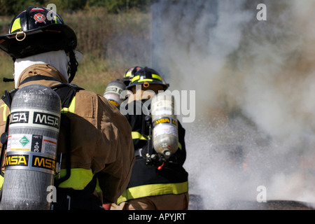 Drei amerikanische Feuerwehrleute unter einem Neuanschluß in den Rauch, das Feuer zu löschen Stockfoto