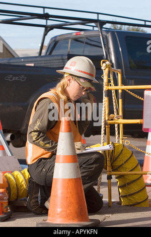 Ein weiblicher Dienstprogramm Arbeiter macht Notizen in ihre Zwischenablage auf der Baustelle mit einem LKW vorbei hinter ihr. Stockfoto