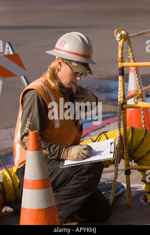 Eine weibliche Dienstprogramm Arbeitskraft verleiht mit ihren Mitarbeitern durch Walkie-Talkie als sie Notizen auf einem Klemmbrett macht. Stockfoto