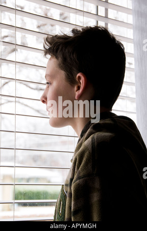 Ein 13-jähriger kaukasischer Junge, der traurig und einsam erscheint, steht vor einem Fenster mit Blick auf die Stadt. USA. Stockfoto