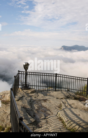 Wolken und Nebel unten ein felsiger Berg Top Beobachtung Punkt mit Münz-Fernglas auf einer eingezäunten Plattform des Felsens. Stockfoto