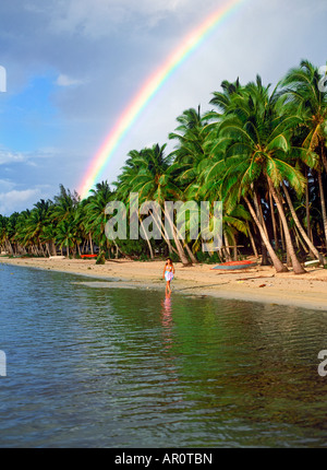 Polynesische Frau zu Fuß unter Regenbogen und Palmen auf Aitutaki Beach in Cook-Inseln Stockfoto