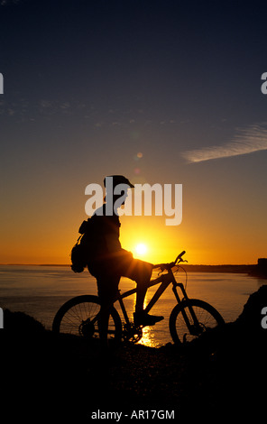 Ein Mountainbiker in der Algarve-Sillhouetted gegen eine untergehende Sonne als He Pause auf den Klippen mit Blick aufs Meer Stockfoto