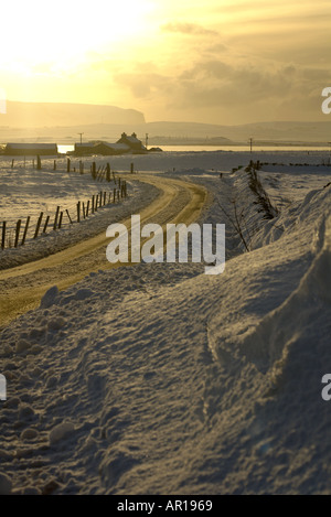 dh Loch of Harray HARRAY ORKNEY Bronze verschneite Straße in der Dämmerung Haus Loch Harray und Stenness Hoy Hills Sonnenuntergang Winter gefrieren Snowfarm uk Farmhouse schottland Stockfoto