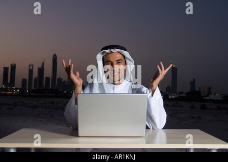 Junge arabische Mann sitzt an einem Schreibtisch - Büro mit Dubai City im Hintergrund Stockfoto