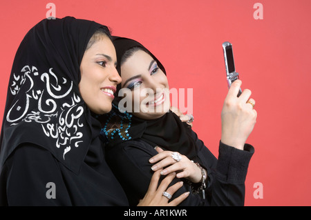 Zwei arabische Damen stehen Wange an Wange mit Handy Stockfoto