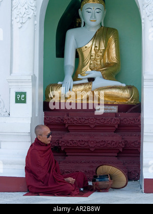 ein Mönch sitzt unter einer Buddha-Statue im Shwedagon Paya Burma s berühmtesten Tempel in Yangon meditiert Stockfoto