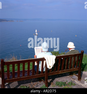 Leute, die auf einer Bank am Meer sitzen und eine Zeitung lesen Tenby South Wales Pembrokeshire UK KATHY DEWITT Stockfoto