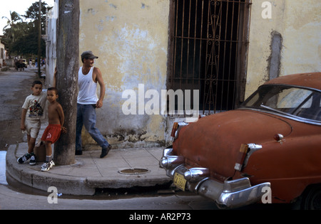 Leben auf der Straße: Mann in weißer Weste zwei Kinder hängen gegen eine Telegraphen-Post und roten klassischen 50er Jahre Auto, Camagüey, Kuba. Stockfoto