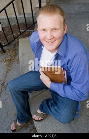 Mann sitzt auf Schritte mit Büchern unter seinem Arm lächelnd Stockfoto