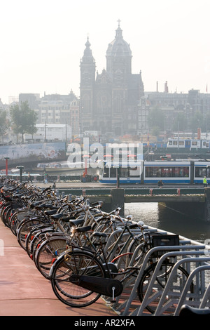 HOLLAND AMSTERDAM BLICK AUF FAHRRÄDER GEPARKT IN MULTI-STOREY-BIKE-PARK MIT STRAßENBAHN REISEN VERGANGENHEIT UND KIRCHE IM HINTERGRUND Stockfoto