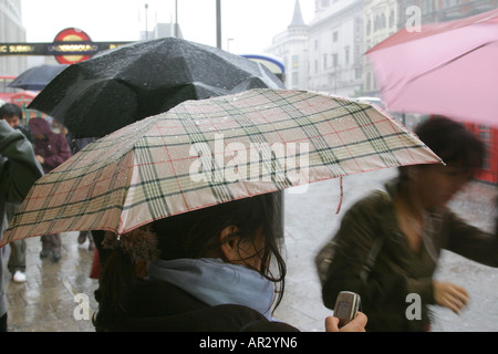 Eine Frau prüft ihr Mobiltelefon einen Regenschirm halten, während ein starker Regenguss Regen, Tottenham Court Road, London, UK. 2006. Stockfoto