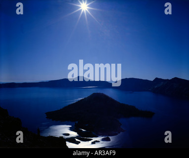 Crater Lake Nationalpark in Oregon mit Wizard Island Silhouette gegen ein Sunburst im frühen Morgenlicht Stockfoto