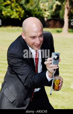 Happy Snapper in Business-Anzug mit Kamera in einer hand und in der anderen trinken Stockfoto