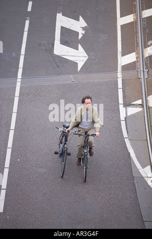 HOLLAND AMSTERDAM DRAUFSICHT DER MANN AUF EINEM FAHRRAD HALTEN EIN ZWEITES FAHRRAD RADFAHREN ÜBER VERGANGENEN ZWEI PFEILE AUF DER STRAßE Stockfoto