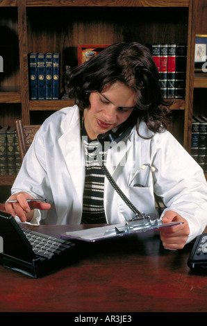 Medizinische Arbeiter Alter 23 Überprüfung Berechnungen auf Handy mit ihrem Laptop-Computer. St Paul Minnesota USA Stockfoto