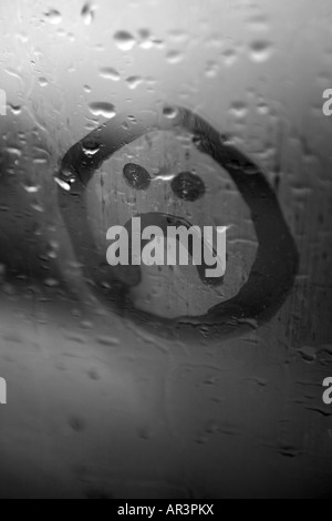 trauriges Gesicht auf die Kondensation in einem verregneten Fenster gezeichnet Stockfoto