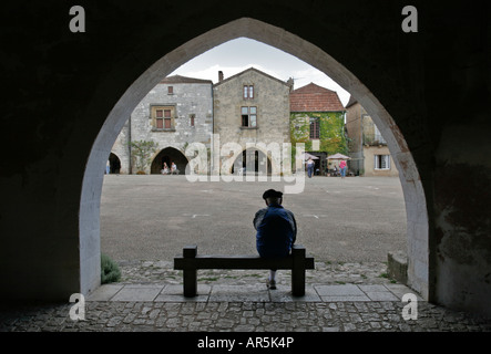 Mann mit Barett sitzt unter einem Bogen in der kleinen Bastide Monpazier in der Dordogne, Frankreich Französisch Stockfoto