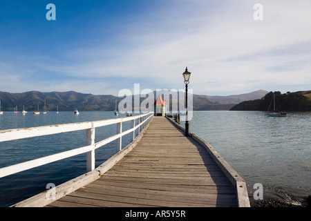 Blick entlang Daly s Wharf mit kleinen roten Dach Gebäude am Ende des hölzernen Steg und Blick über Hafen in der Bucht Akaroa Neuseeland Stockfoto