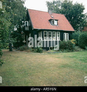 Rasen vor kleinen schwedischen Häuschen mit rotem Dach und schwarzen Wände mit weißen Fenster Stockfoto