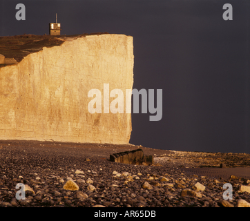 Birling Gap Klippe Gesicht beleuchtet von der Sonne sehr dunkel Himmel und Kies-Strand Stockfoto