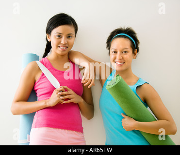 Zwei junge Frauen stehen in Trainingskleidung hält Yoga-Matten und lächelnd Stockfoto