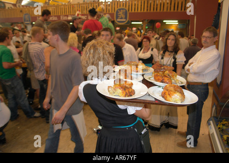 Server-Kellnerin tragen Tablett mit Brathähnchen oder gebratenem Fleisch um im Bierzelt auf Oktoberfest Bier Festival Stockfoto