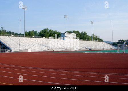 American football stadium with white bleachers and a red running track, which is empty in the sunlit morning. The field is lined with stadium lights. Stockfoto