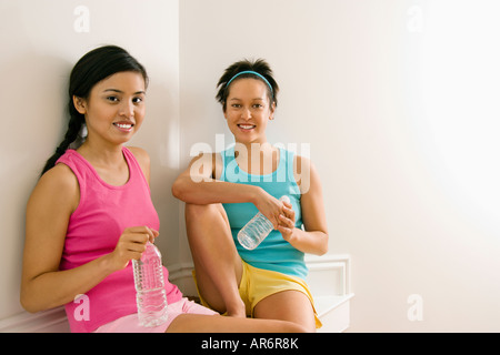 Zwei junge Frauen in Fitness Kleidung mit Wasserflaschen sitzen, Lächeln Stockfoto