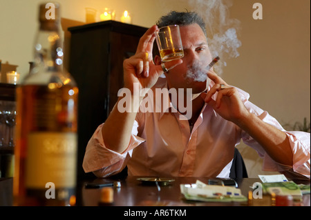 Mann an einem Tisch mit Whiskey, raucht eine Zigarre Stockfoto