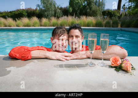 Vollständig bekleidet schwules Paar trinken Champagner im Schwimmbad Stockfoto