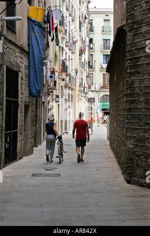 Zwei Personen, eins mit dem Fahrrad, zu Fuß in einer engen Straße in Barcelona, Spanien Stockfoto