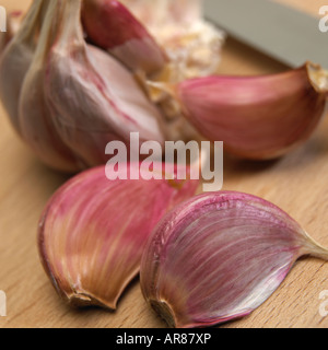 NAHAUFNAHME VON KNOBLAUCHZWIEBEL UND NELKEN MIT KÜCHENMESSER AUF HOLZTISCH Stockfoto