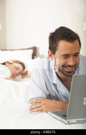 Paar im Bett, Mann mit Laptop Stockfoto