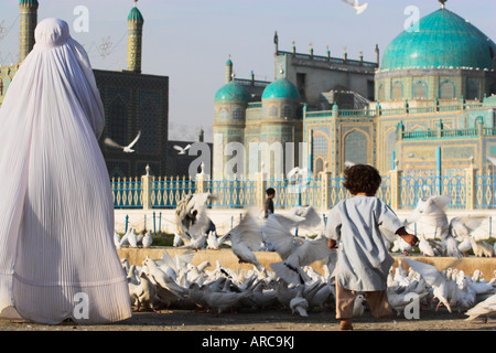 Lady in Burka, die berühmten weißen Tauben zu füttern, während Kind sie Schrein von Hazrat Ali, Mazar-i-Sharif, Balkh, Afghanistan jagt Stockfoto