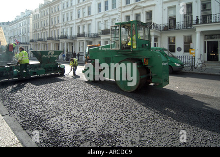 Contra Jour gegen Tageslichtbeleuchtung an Männern und Maschinen bei der Arbeit mit großer Walze, die eine neue Asphaltstraße in South Kensington London England verlegt Stockfoto