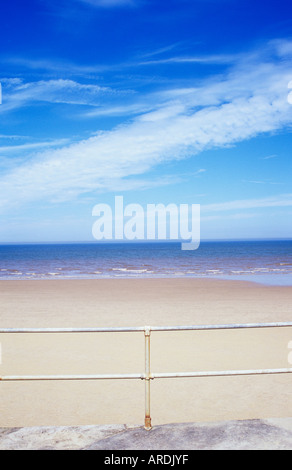 Blick von der Promenade über Geländer zu einem weiten leeren Sandstrand und entfernte ruhige blaue Meer und Himmel Stockfoto