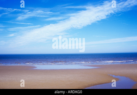 Blick auf weiten leeren Sandstrand mit einigen Patches noch liegen Meerwasser und entfernte ruhige blaue Meer und Himmel Stockfoto