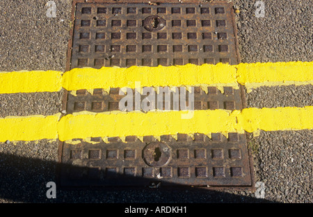 Detail von oben der frisch gestrichene doppelte gelbe Linien kreuzen ein Quadrat Metall Schachtdeckel inmitten einer Asphaltstraße Stockfoto