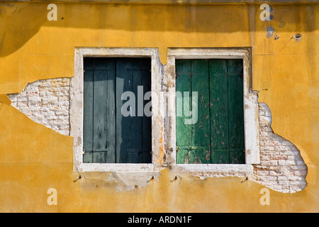 Zwei Fensterläden mit abblätternde Farbe inmitten Stuck bedeckt Mauer benötigt eine Reparatur und Überholung von Venedig Italien Stockfoto