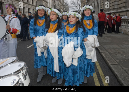 Junge Cheerleader für Hawaian Highschool-Band in blauen Kleidern mit Blume Stirnbänder und Lei halten weiße Kitteln auf Street in London Stockfoto