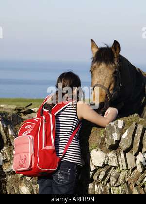 Junge Mädchen tragen einen Rucksack, ein Pferd über eine Steinmauer streicheln Stockfoto